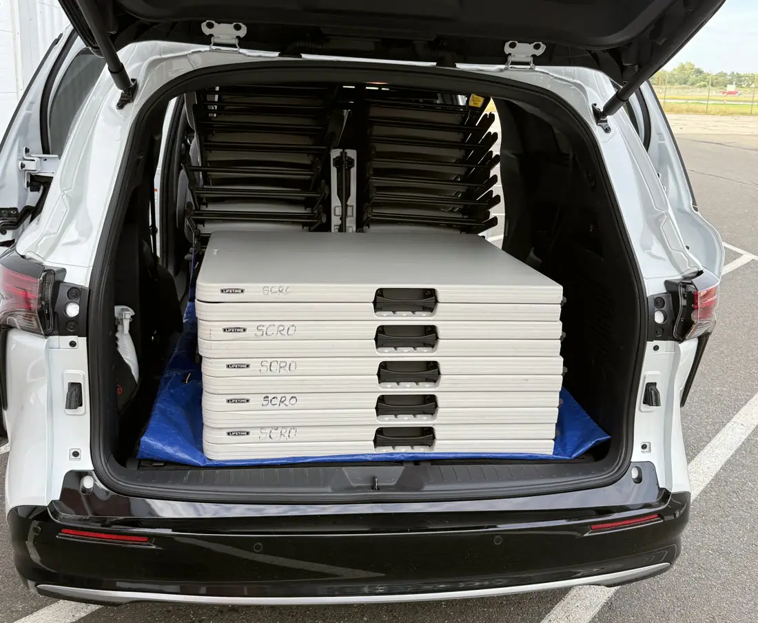 Five folded rental tables stacked in the back of the delivery vehicle, chairs racked behind them