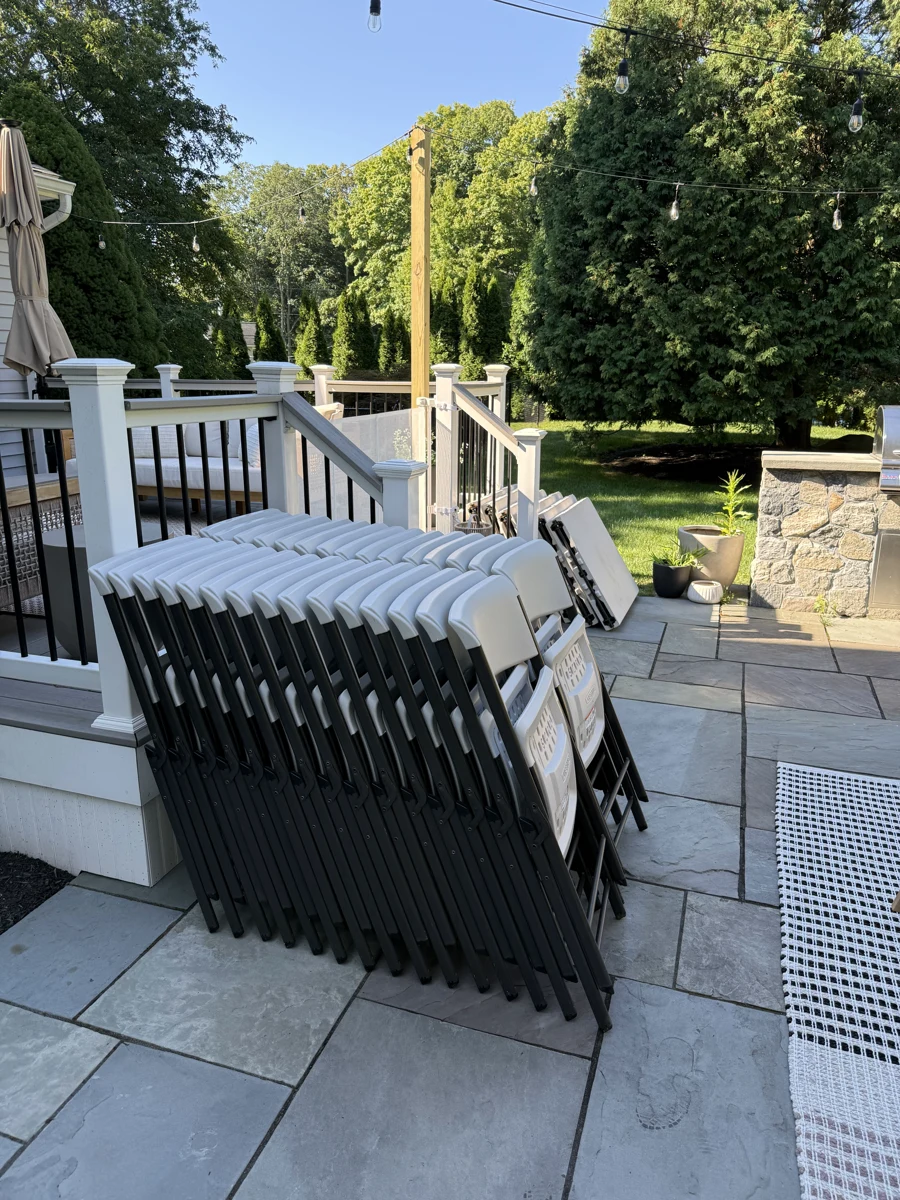 White folding chairs and tables delivered beside a patio with string lights