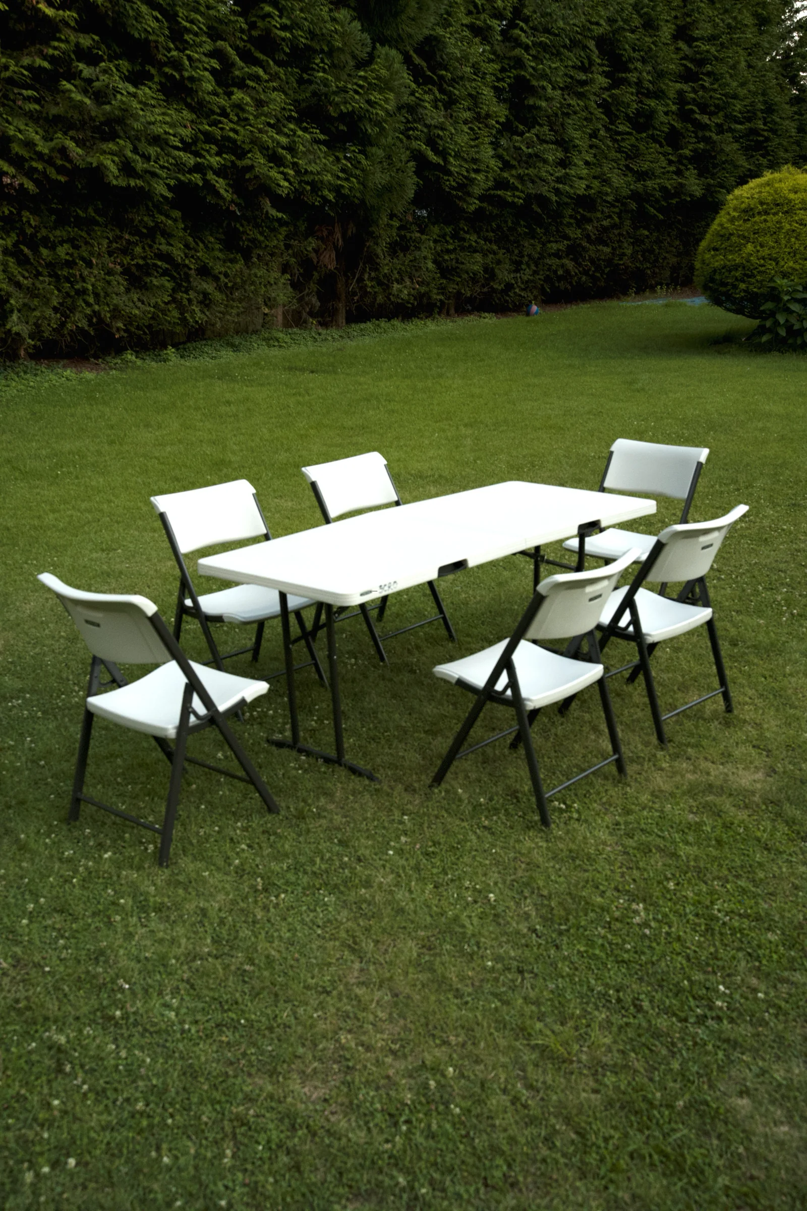 White folding table and chair set on a bright green backyard lawn, ready for a party