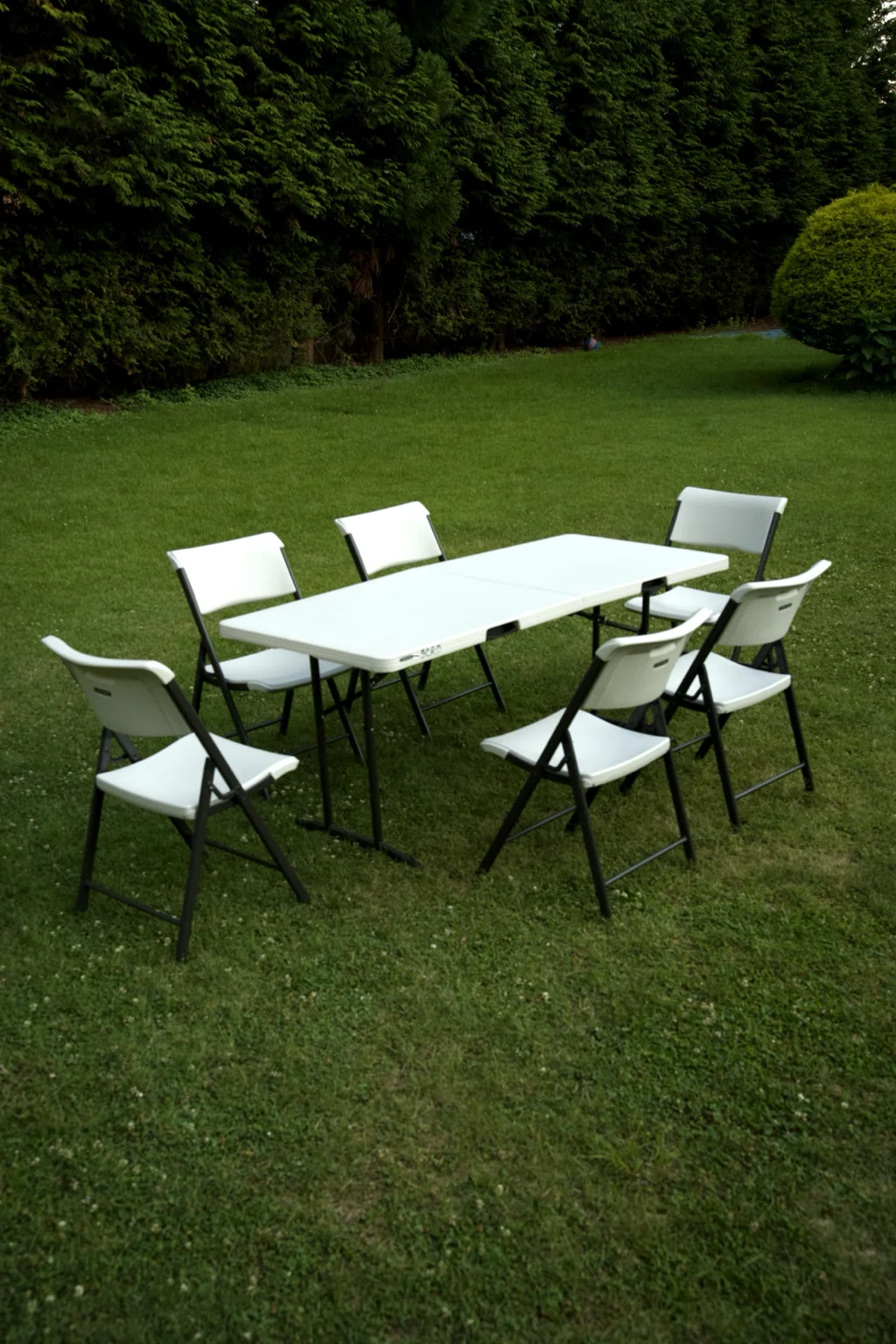 Rental folding table and six chairs arranged on a hedge-lined Connecticut backyard at dusk
