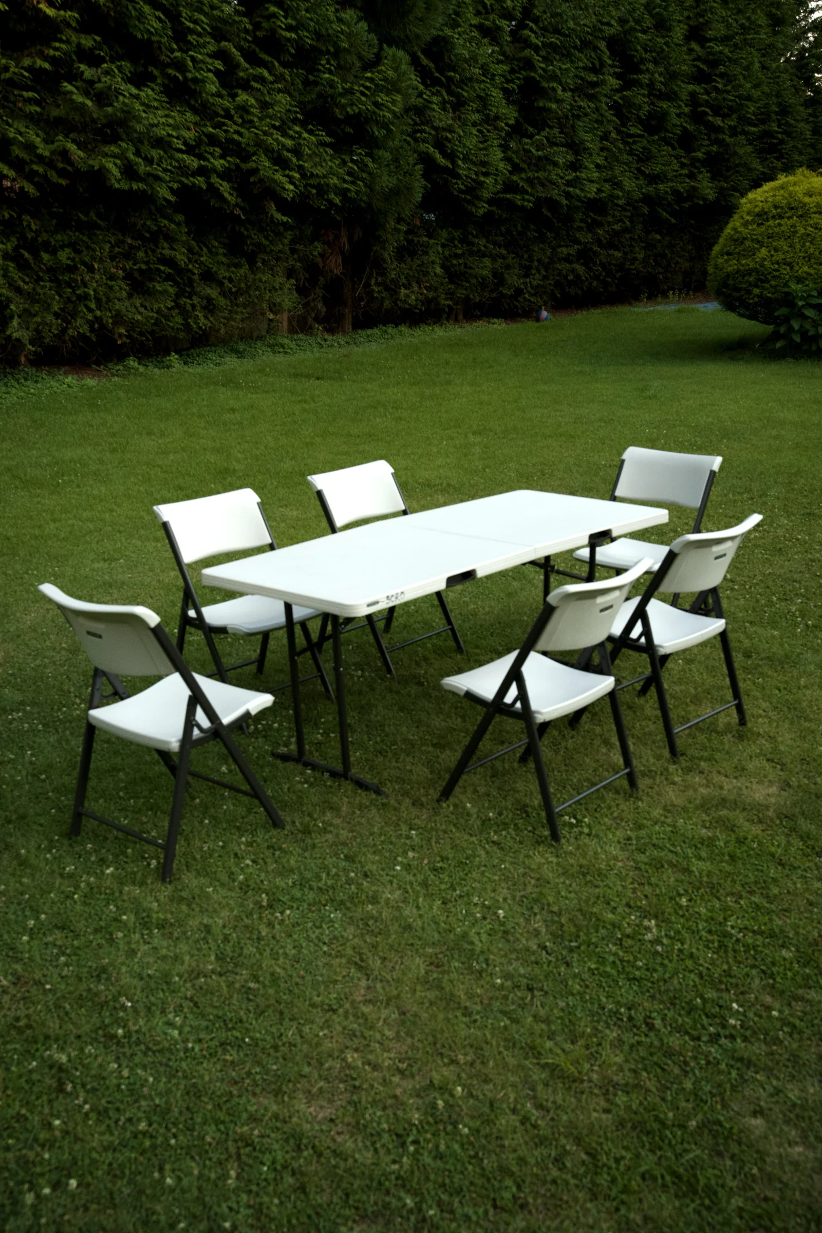 Rental folding table and six chairs arranged on a hedge-lined Connecticut backyard at dusk