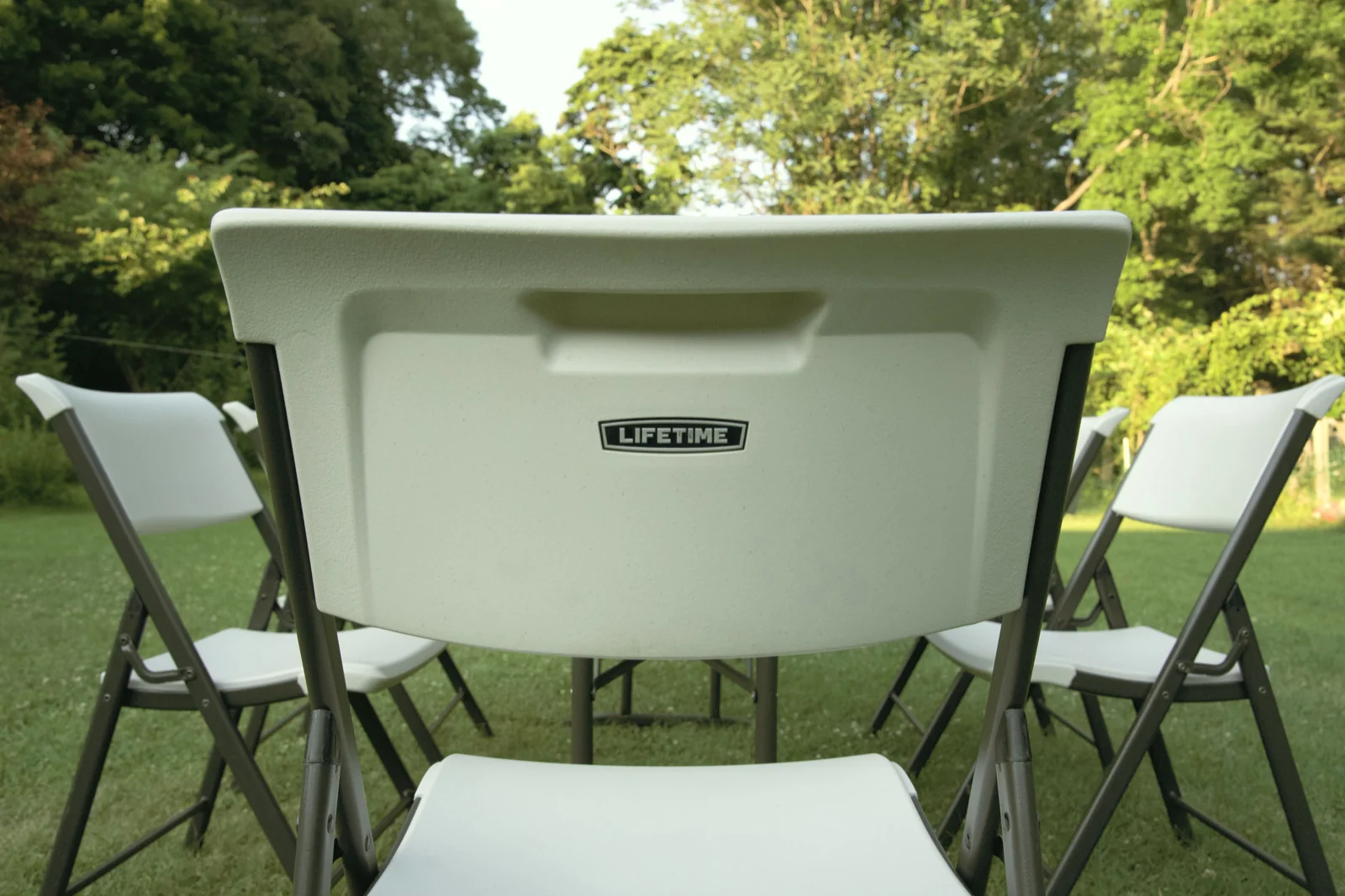 Circle of white folding chairs on a lawn in warm evening light