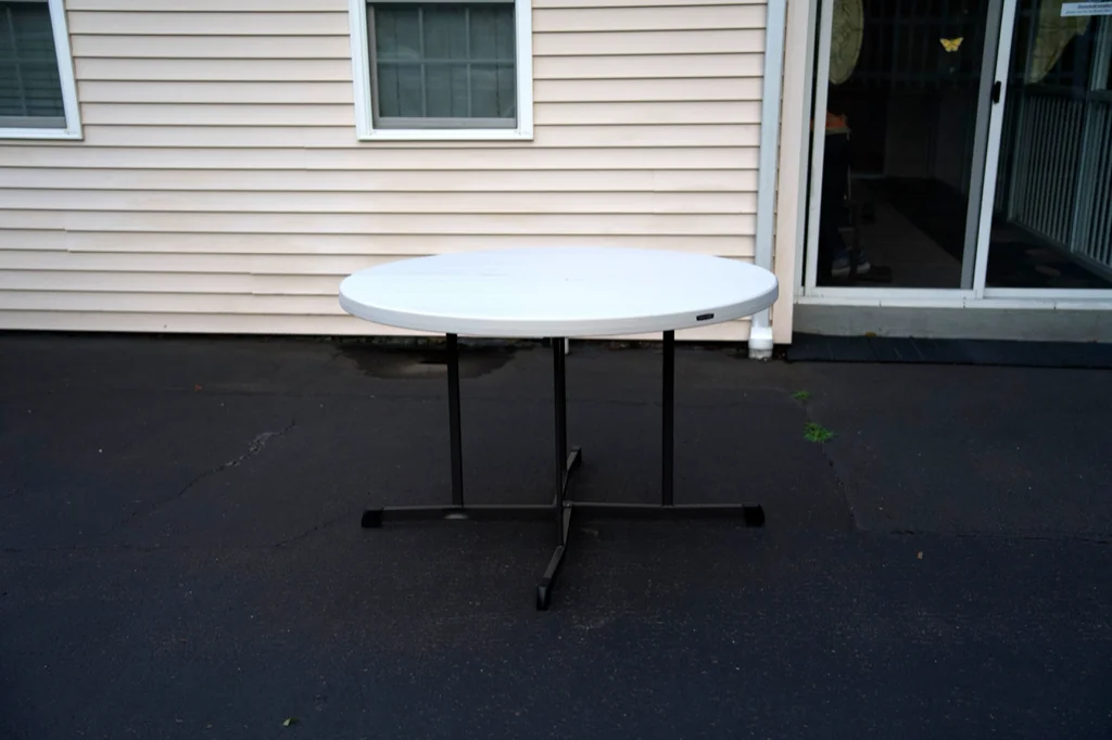48-inch round fold-in-half table set up outdoors beside a stack of folded rounds