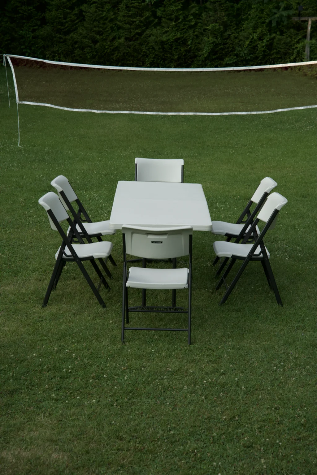 Card table with folding chairs set on a lawn in front of a volleyball net