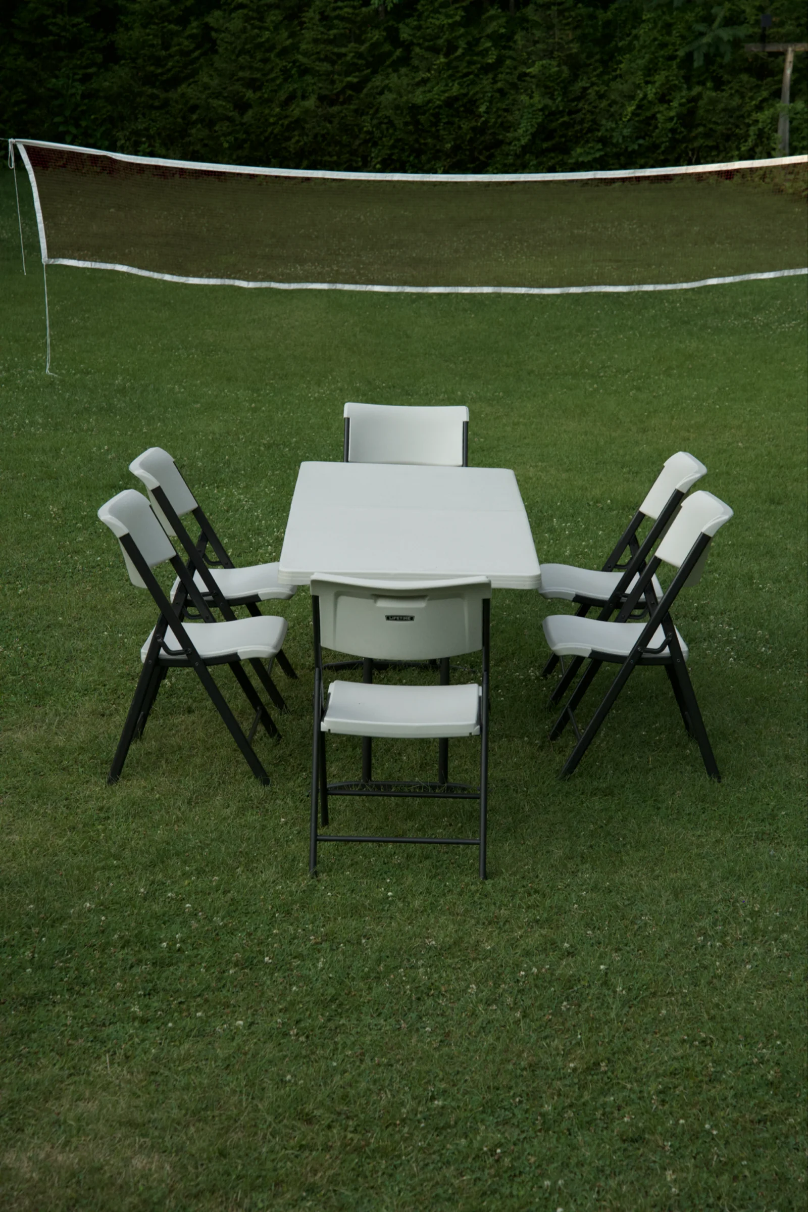Card table with folding chairs set on a lawn in front of a volleyball net