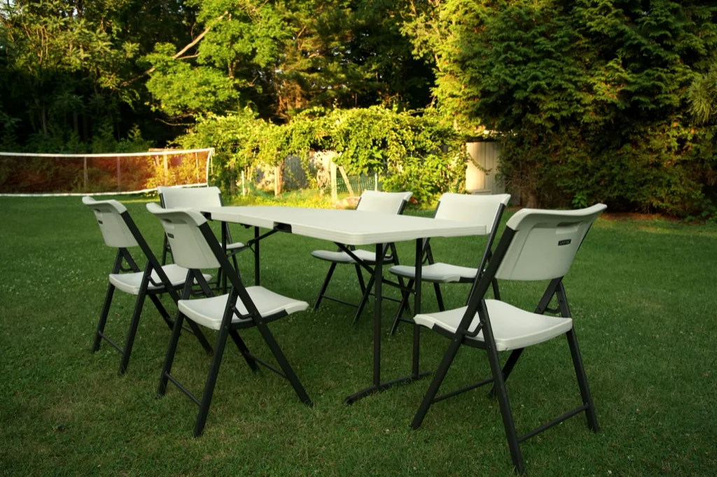 Six-foot folding table with six white folding chairs set up on a Connecticut backyard lawn at golden hour